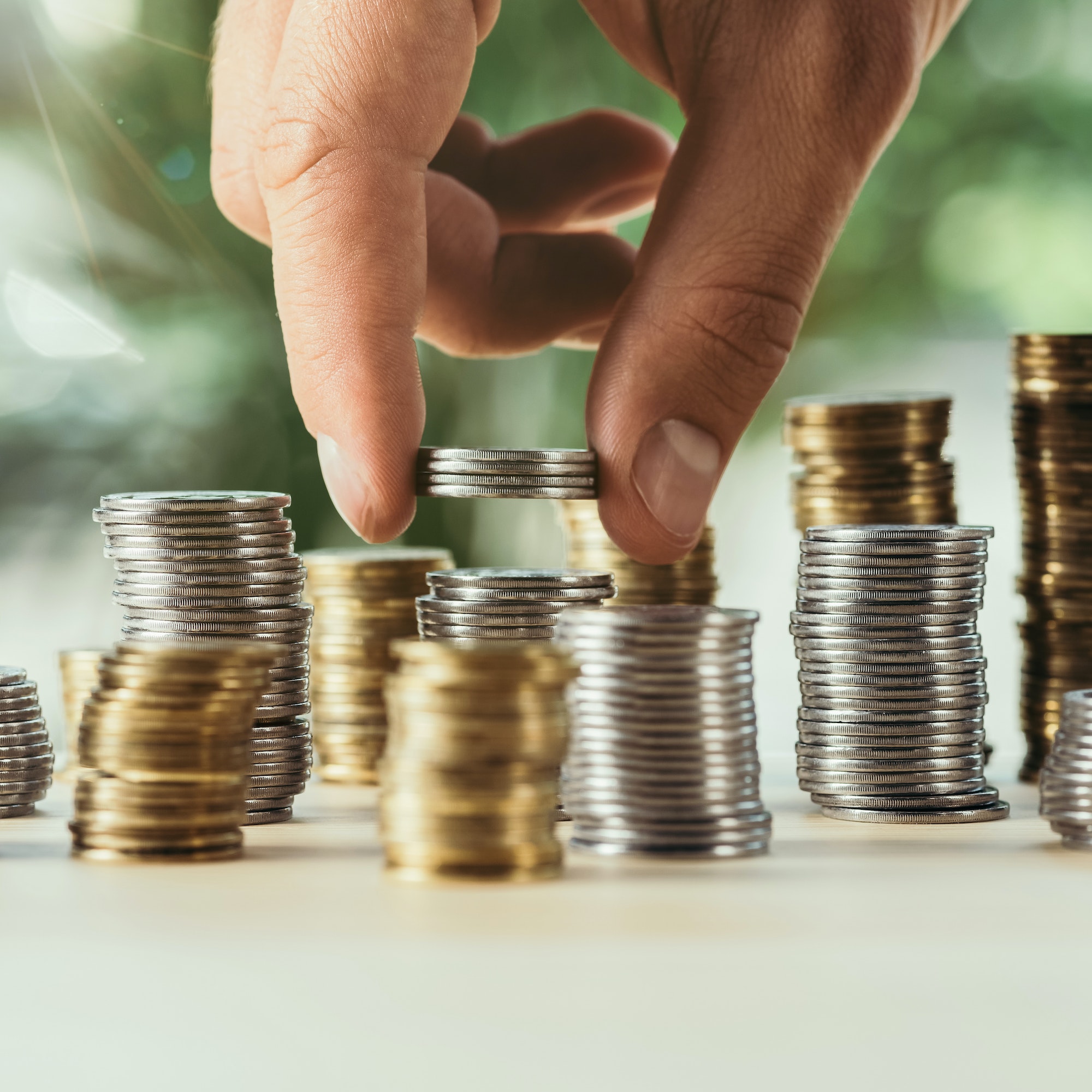 cropped view of person stacking coins on table on blurred green background