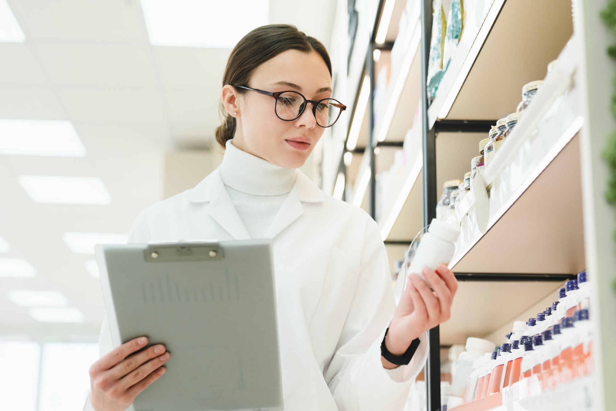 Druggist holding remedy pills, learning new medicines goods with clipboard on shelves of pharmacy
